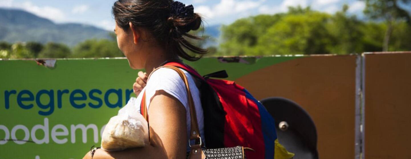 Une femme latino-américaine portant un sac à dos et des sacs se promène à l'extérieur, avec des montagnes en arrière-plan.