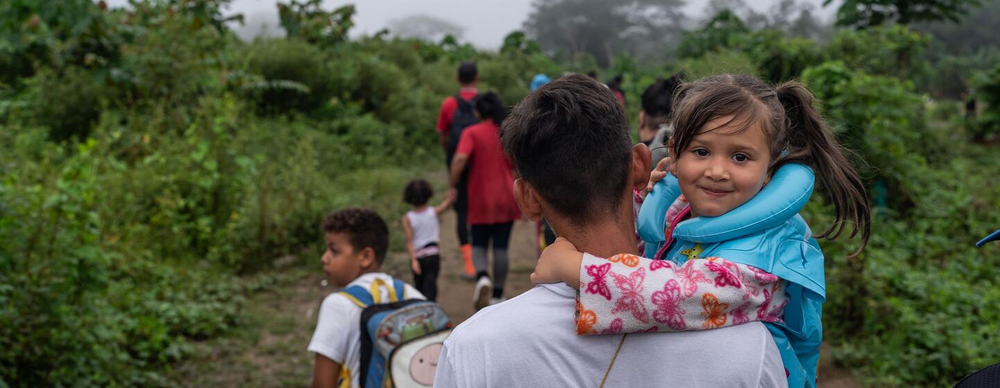 Un père vénézuélien migrant porte sa jeune fille sur ses épaules alors qu'ils empruntent un sentier en jungle avec d'autres migrants devant eux.