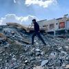 صبي فلسطيني يمشي على أنقاض المنازل المدمرة في غزة، مع مبان متضررة في الخلفية.
