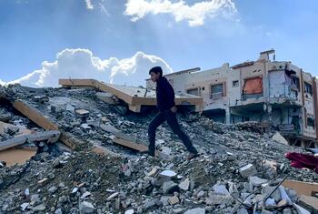 صبي فلسطيني يمشي على أنقاض المنازل المدمرة في غزة، مع مبان متضررة في الخلفية.