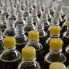 Des rangées de bouteilles en plastique pour sodas avec des bouchons jaunes, certaines ouvertes et d'autres fermées, remplies de liquide gazeux foncé.