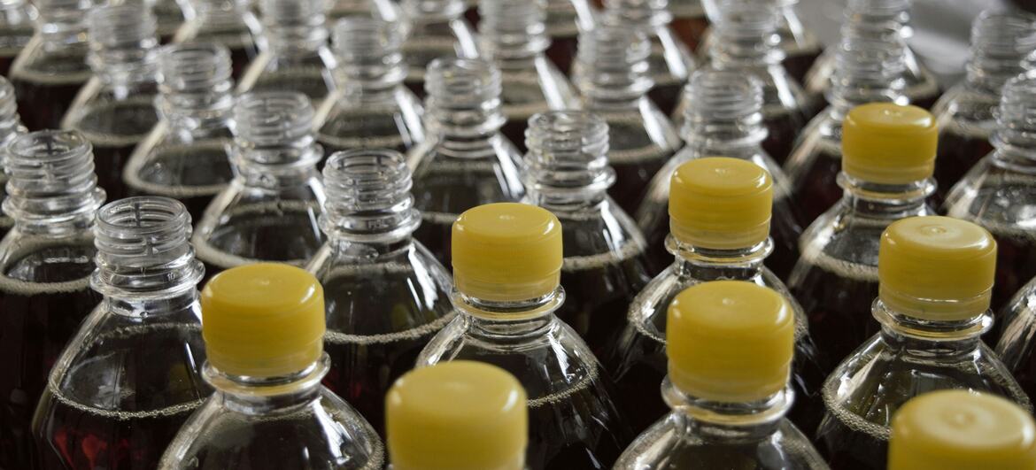 Filas de botellas de plástico para refrescos con tapas amarillas, algunas abiertas y otras cerradas, llenas de líquido carbonatado oscuro.