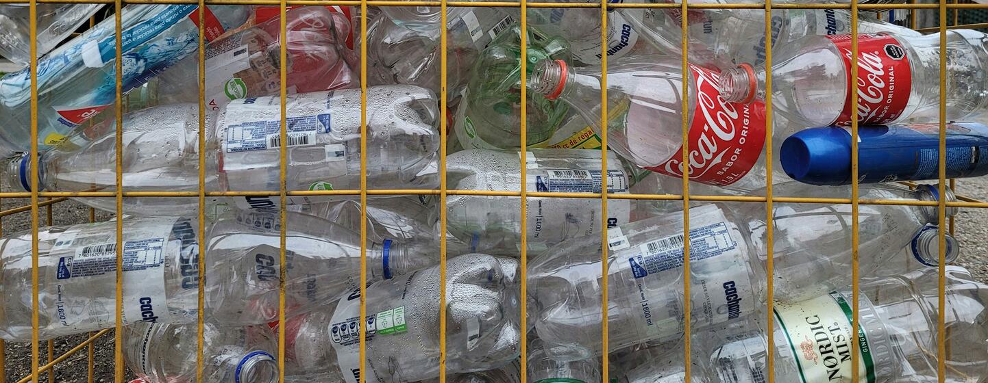 Une cage métallique remplie de diverses bouteilles en plastique, notamment des contenants de Coca-Cola et d'eau minérale, dans un centre de recyclage.