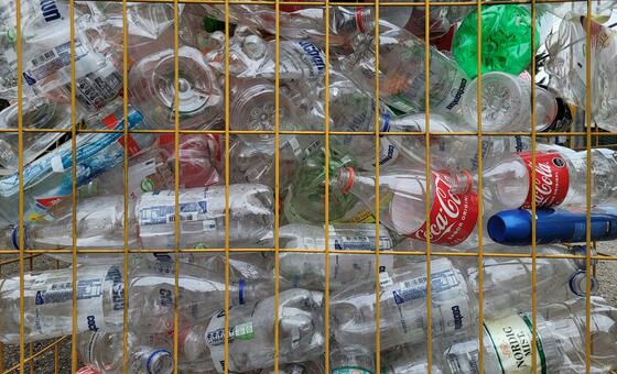 Une cage métallique remplie de diverses bouteilles en plastique, notamment des contenants de Coca-Cola et d'eau minérale, dans un centre de recyclage.
