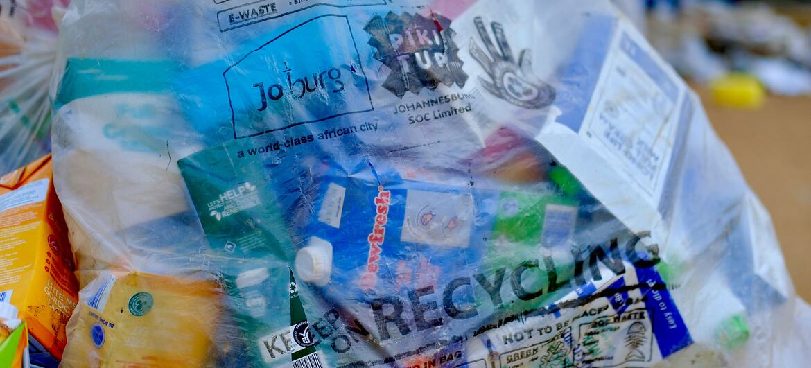 A clear plastic recycling bag filled with various recyclable items including plastic bottles, cartons, and containers, with a Johannesburg recycling guide visible on the bag.