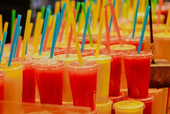 Rows of colorful drinks in plastic cups with plastic straws.