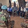 جنود حفظ السلام الأمم المتحدة في جنوب السودان يتواصلون مع المدنيين النازحين في مخيم بمنطقة تامبورا الكبرى. يجلس الجنود، مرتدين خوذات الأمم المتحدة ، في دائرة مع أفراد المجتمع المحلي على أرض ترابية.