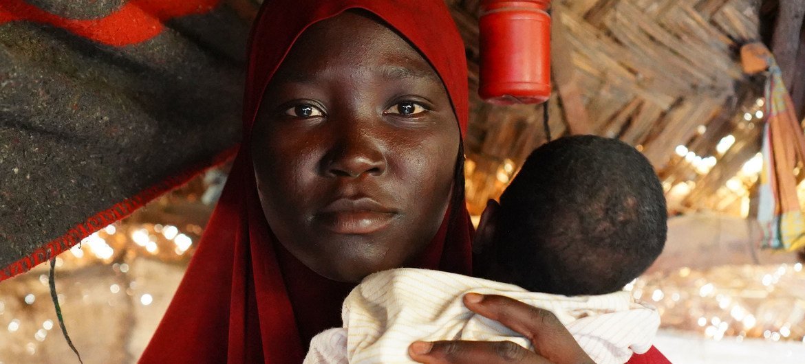 在尼日利亚东北部迈杜古里，一名妇女抱着她的婴儿，帽子是为流离失所者准备的。