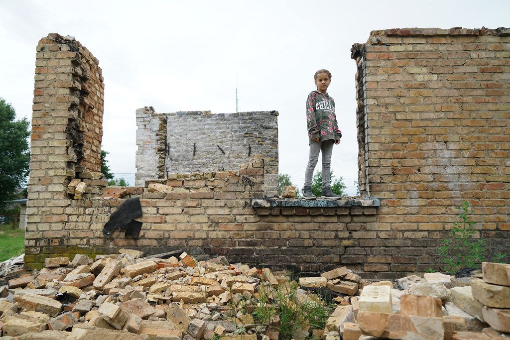 Une jeune fille posant devant les décombres de son école, dans la banlieue de Kïyv, en Ukraine. (archives) ​