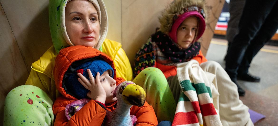أم وابنتها وابنها يجلسون على الأرض في محطة مترو الأنفاق في كييف ليحتموا من القصف.