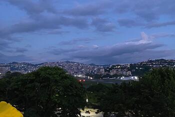Una vista del crepúsculo de Caracas, Venezuela, mostrando el horizonte iluminado de la ciudad, las colinas circundantes y una pista de aterrizaje del aeropuerto en primer plano.