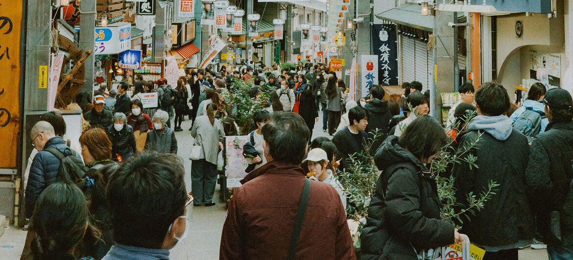 A bustling shopping mall in Japan filled with people walking between shops and street vendors, showcasing a vibrant retail district.