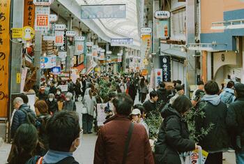 A bustling shopping mall in Japan filled with people walking between shops and street vendors, showcasing a vibrant retail district.