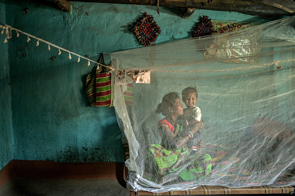 Una mujer y un niño sentados bajo un mosquitero en Chhattisgarh, India.