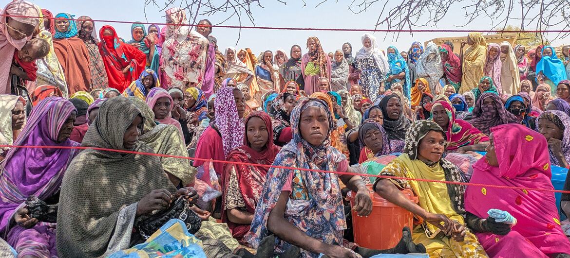 تتلقى مجموعة من النساء والأطفال السودانيات اللاجئات المساعدة الغذائية في مخيم كولبوس للاجئين في تشاد، بدعم من برنامج الأغذية العالمي (WFP). يجلسون تحت الأشجار، يحملون أكياسًا من المواد الغذائية بما في ذلك الخضروات والأطعمة المغذية المتخصصة للأمهات والأطفال.