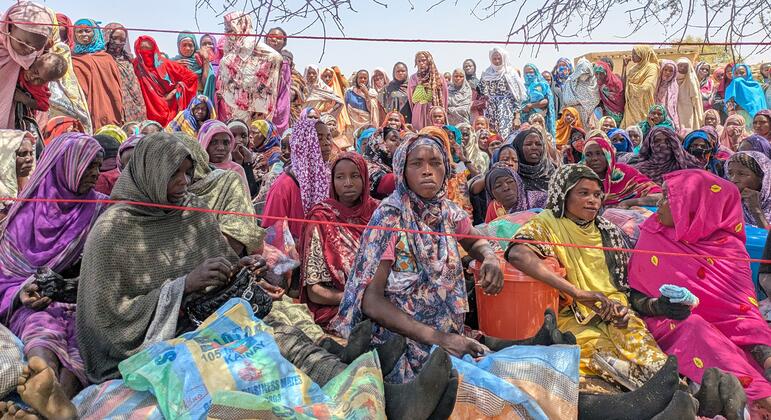 Kikundi cha wanawake wa wakimbizi wa Sudan na watoto wanapokea msaada wa chakula katika kituo cha wakimbizi cha Koulbus nchini Chad, wakiungwa mkono na Shirika la Chakula Duniani (WFP).Wao wameketi chini ya miti, wakiwa na mifuko ya vyakula ikiwa ni pamoja na sorghum na vyakula maalum vyenye lishe kwa akina mama na watoto.