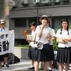 Un groupe d'élèves du secondaire japonais en uniforme participe à une manifestation ou à une manifestation, tenant des pancartes et utilisant un mégaphone pour parler.