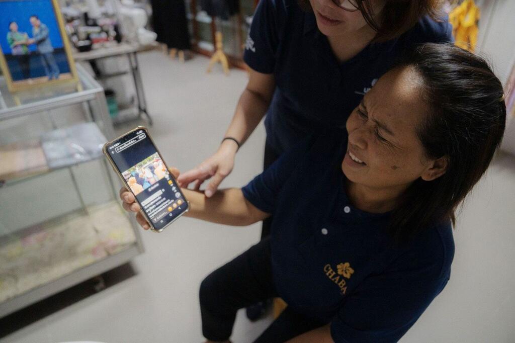 A Thai woman cries while looking at a video call on her smartphone, supported by another woman.