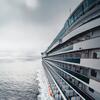 A large white cruise ship sails across the ocean on a cloudy day.