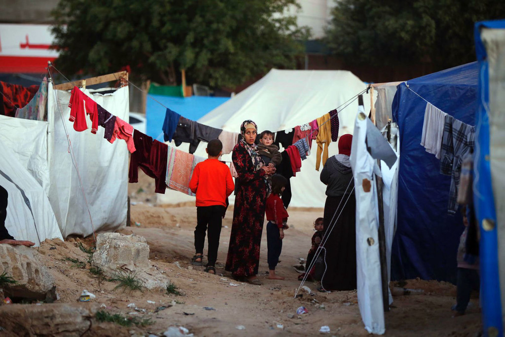 Una mujer sostiene a un niño en brazos en un campamento de tiendas de campaña en Gaza.