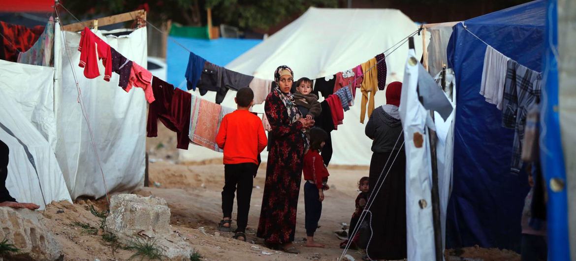 Une femme tient un enfant dans ses bras dans un camp de tentes à Gaza.