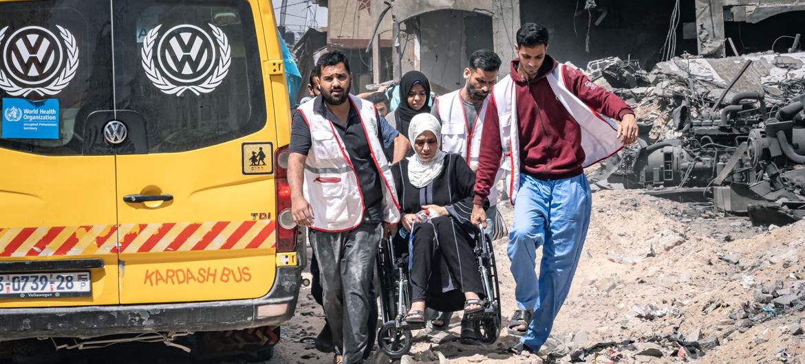 A woman in a wheelchair is carried across rubble. A woman in a wheelchair is carried across rubble.