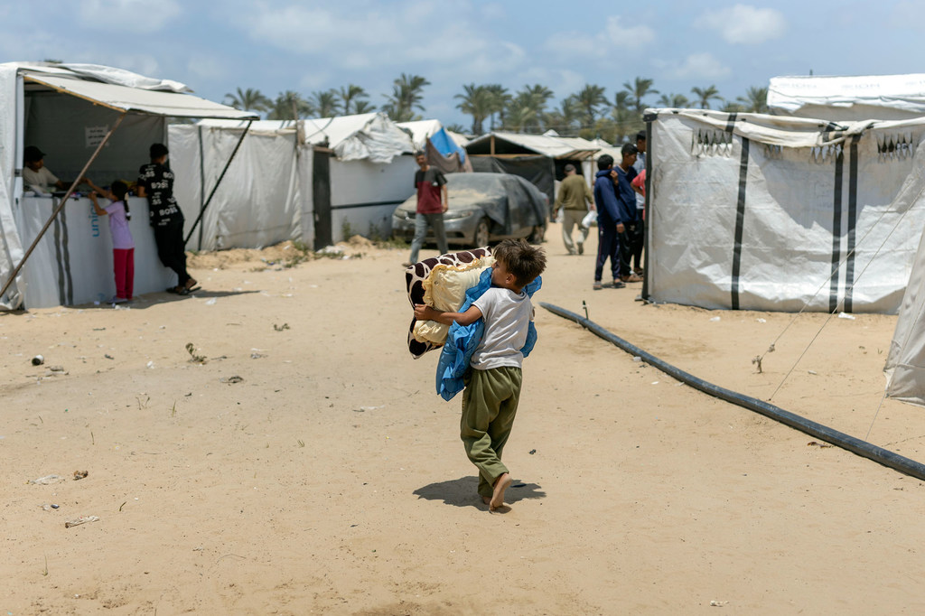 Un niño lleva sus pertenencias en el campo de desplazados de Al Mawasi, en Gaza.