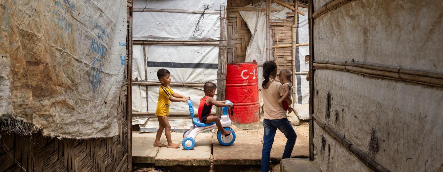 Des enfants jouent sur un tricycle dans une ruelle étroite entre des abris d'un camp de réfugiés rohingyas à Cox's Bazar, au Bangladesh.