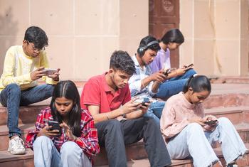 Indian teenagers sitting on steps in Delhi using mobile phones.