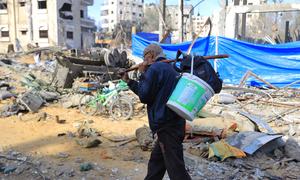 Un hombre camina con sus pertenencias a cuestas en medio de las ruinas y la basura en Gaza.