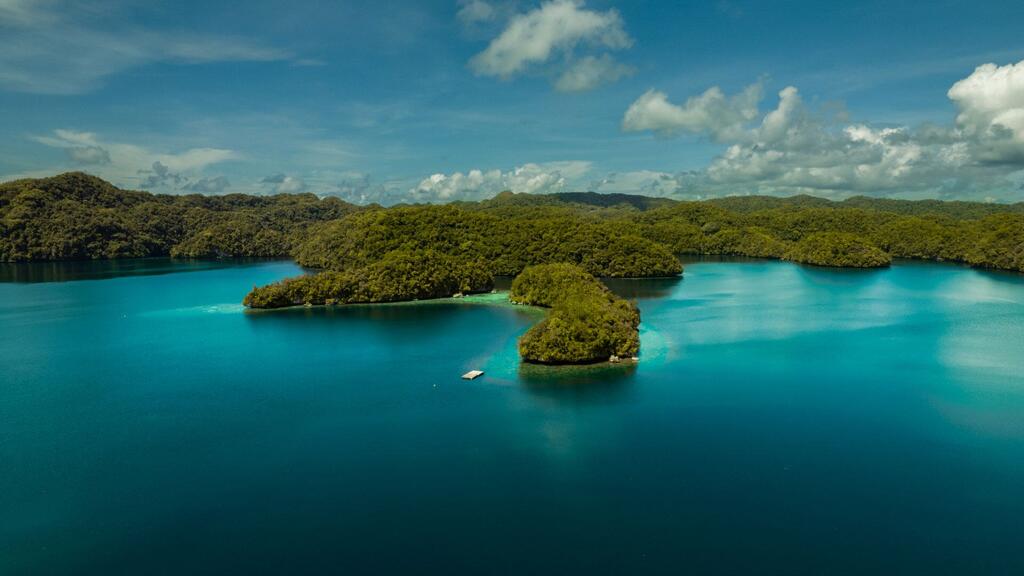Aerial view of Palau, a tropical island in the Pacific Ocean, showcasing lush green forests, clear blue waters, and coral reefs, highlighting the island's natural beauty and the importance of disaster resilience.