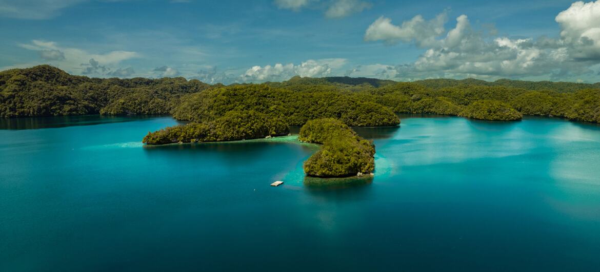 Vista aérea de Palau, uma ilha tropical no Oceano Pacífico, mostrando florestas verdes exuberantes, águas azuis claras e recifes de coral, destacando a beleza natural da ilha e a importância da resiliência a desastres.
