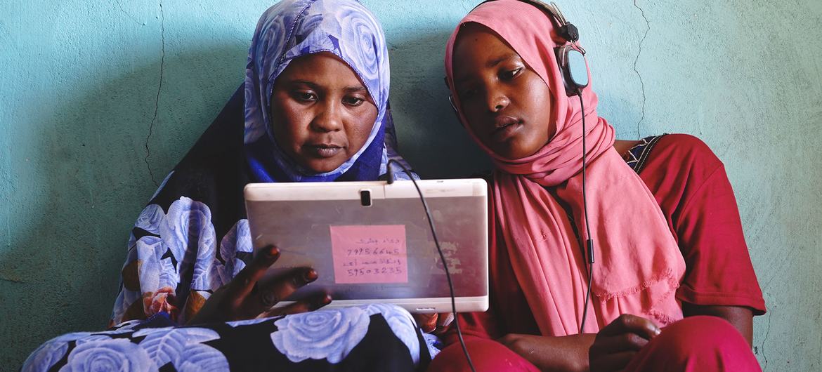 Two young women in Sudan play educational games on a solar-powered tablet. 