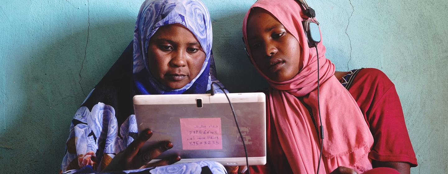 Deux jeunes filles soudanaises jouent à des jeux éducatifs sur une tablette à énergie solaire.
