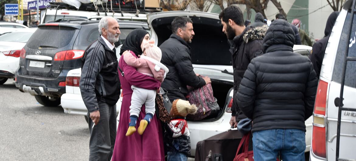 Refugee family with luggage waits at the Masnaa border crossing in Lebanon to enter Syria, escaping Israeli bombing.