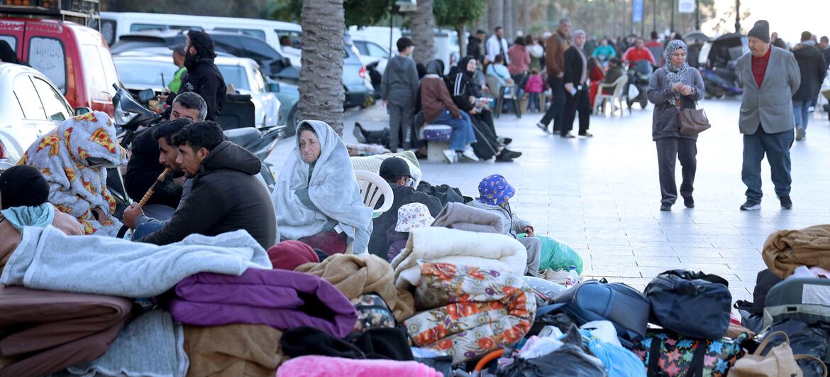 Displaced families, including children and adults, sit on a street in Beirut, Lebanon, surrounded by their belongings and blankets following evacuation warnings.
