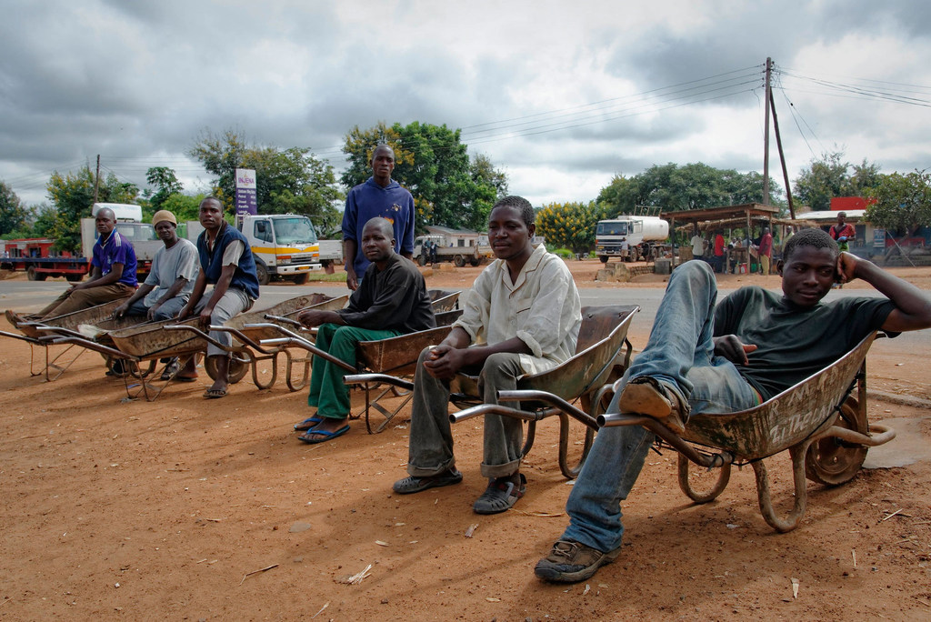 Un grupo de hombres africanos esperan trabajo, sentados en carretillas al borde de una carretera en Kasungu, Malawi.