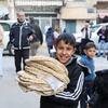 Un jeune garçon syrien souriant tient une grande pile de pain plat frais à l'extérieur d'une boulangerie à Jdeideh Al-Fadel, en Syrie, où le Programme alimentaire mondial (PAM) a réhabilité l'installation pour améliorer la sécurité alimentaire de la population locale.