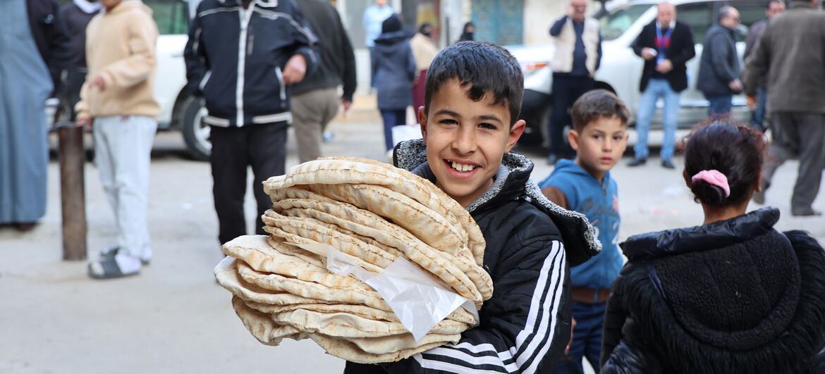 Un jeune garçon syrien souriant tient une grande pile de pain plat frais à l'extérieur d'une boulangerie à Jdeideh Al-Fadel, en Syrie, où le Programme alimentaire mondial (PAM) a réhabilité l'installation pour améliorer la sécurité alimentaire de la population locale.