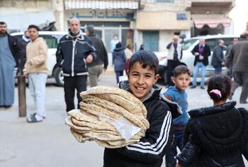 صبي سوري مبتسم يحمل كومة كبيرة من الخبز الرقيق الطازج خارج مخبز في جدة الفدل، سوريا، حيث قام برنامج الأغذية العالمي (WFP) بإعادة تأهيل المنشأة لتحسين الأمن الغذائي للسكان المحليين.