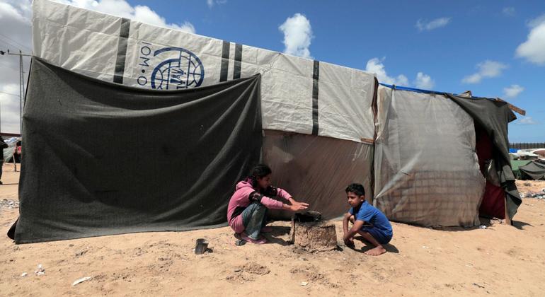 Duas crianças brincam do lado de fora de um abrigo em Gaza feito com materiais variados, inclusive da ONU