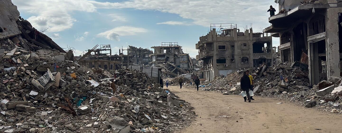Détruction à Jabalya, dans le nord de Gaza, avec des gens marchant dans des rues dévastées et des bâtiments endommagés sous un ciel partiellement nuageux.