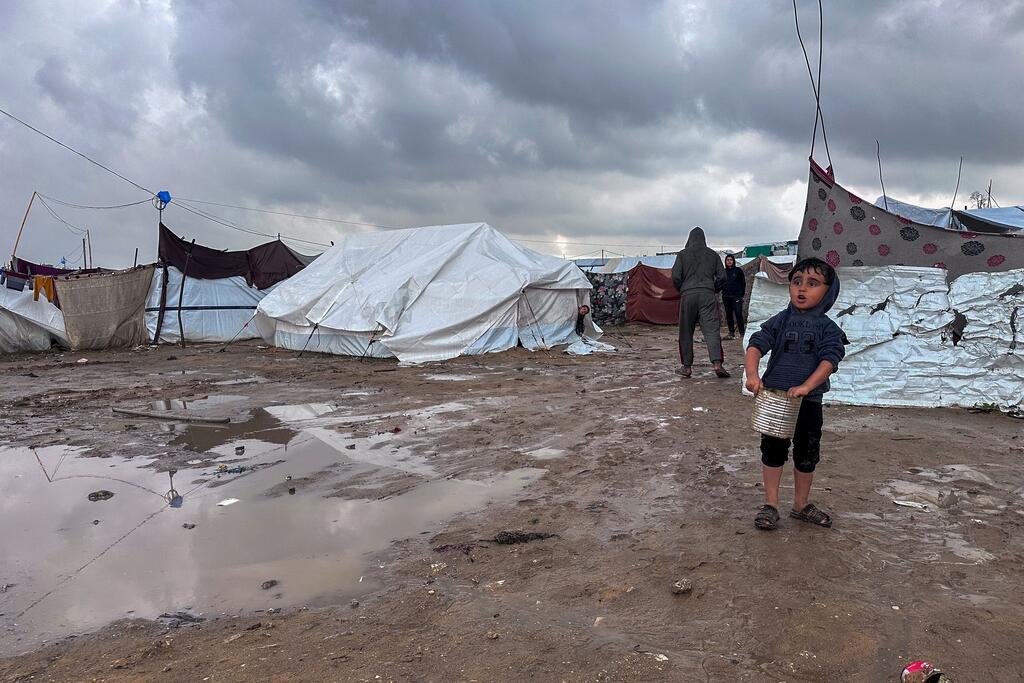 一个男孩拿着一个桶站在加沙北部贾巴利亚的一个泥流离失所者营地里。