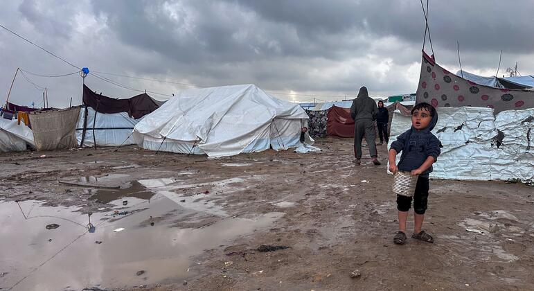 Un niño se encuentra en un barroco campamento de desplazados en Jabalya, en el norte de Gaza, sosteniendo un cubo.