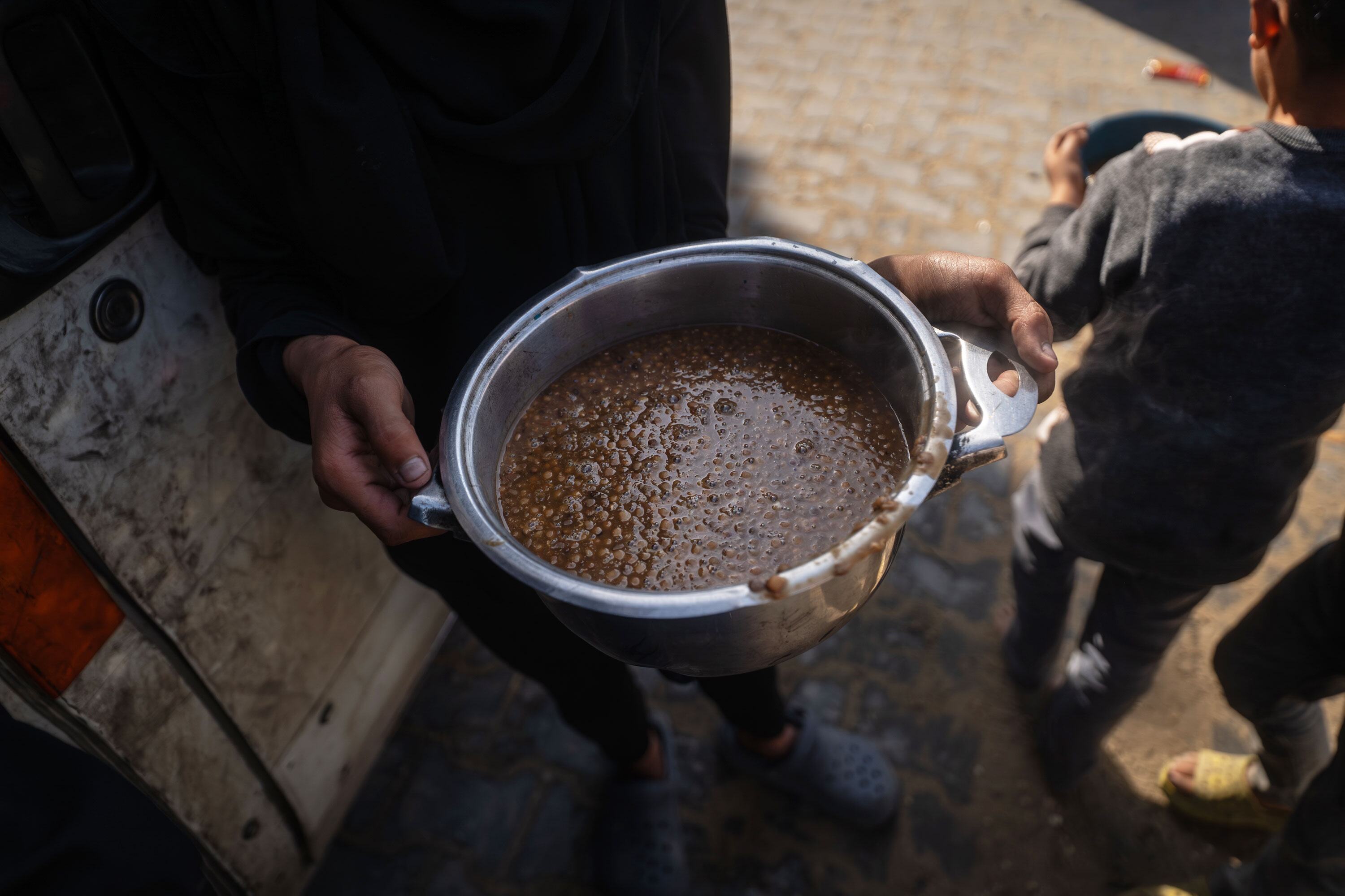 Une personne distribue un repas chaud à partir d'un pot métallique aux enfants de Khan Younis, à Gaza, dans le cadre des efforts humanitaires soutenus par le PAM.