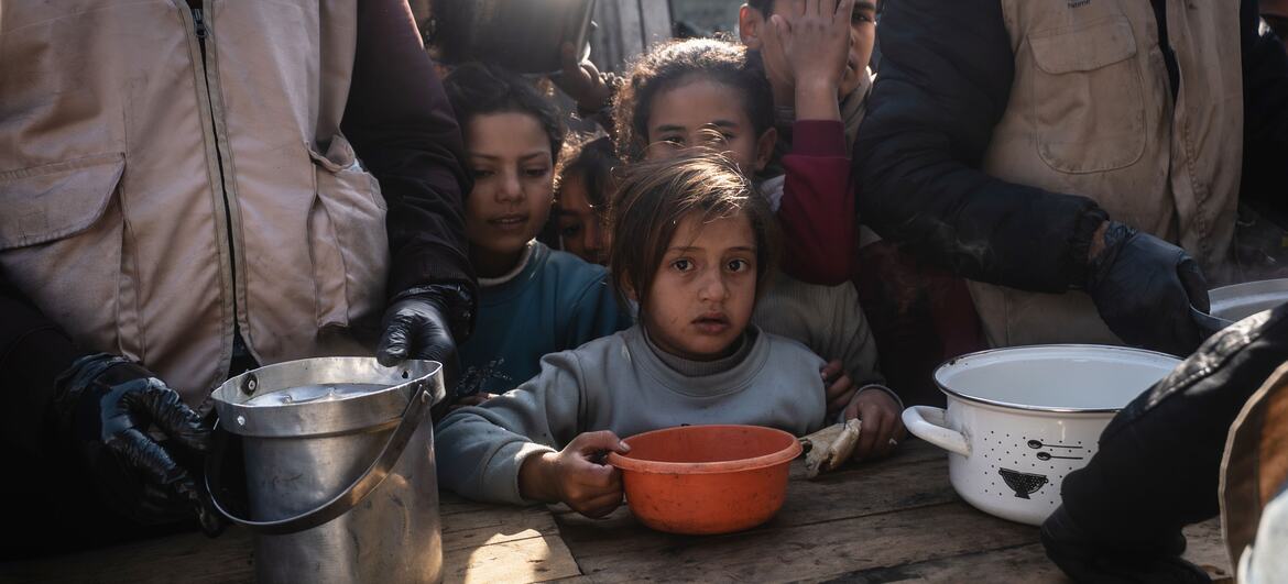 Children receive food aid from World Food Programme workers at a distribution center in Khan Younis, Gaza, where meals are provided to families affected by the war.