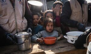 Children receive food aid from World Food Programme workers at a distribution center in Khan Younis, Gaza, where meals are provided to families affected by the war.