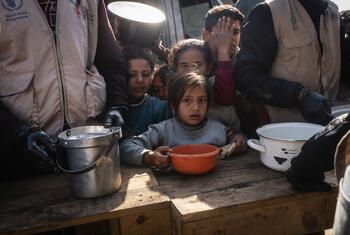 Children receive food aid from World Food Programme workers at a distribution center in Khan Younis, Gaza, where meals are provided to families affected by the war.