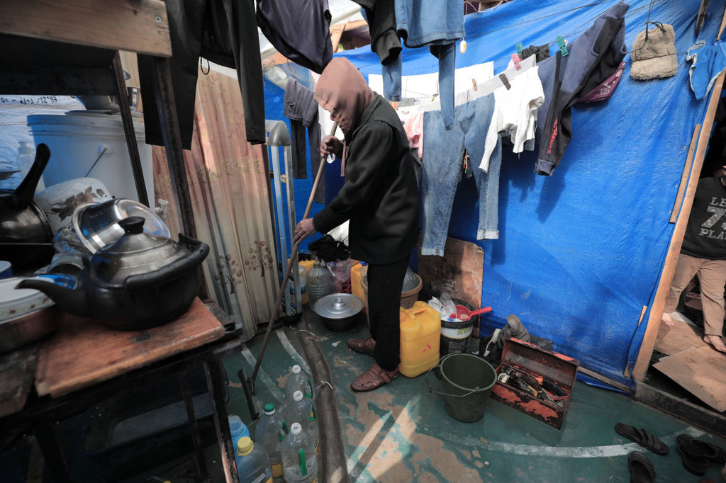 Une personne balaie le sol à l'intérieur d'une tente bondée dans un camp de déplacés touché par les inondations à Rafah, dans la bande de Gaza.