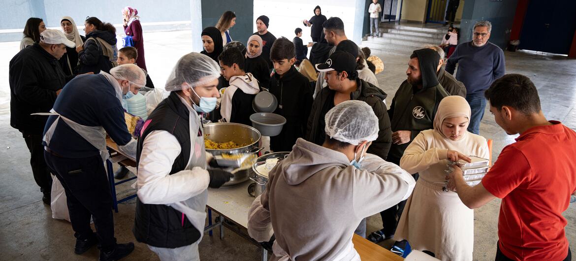 Voluntarios con redes para el cabello y máscaras sirven comidas calientes desde grandes tazones a familias desplazadas en un centro comunitario en el Líbano, como parte de un esfuerzo de ayuda del Programa Mundial de Alimentos (PMA).